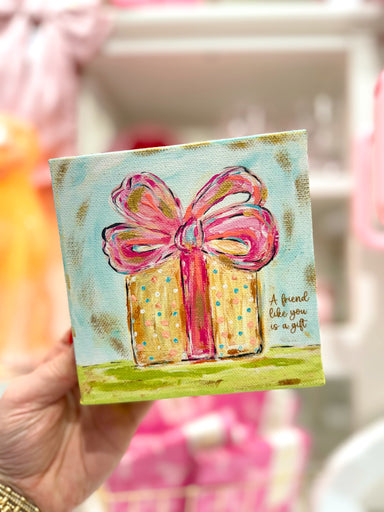 A canvas decor with a colorful present and a bow on it, with text that reads 'A friend like you is a gift'.