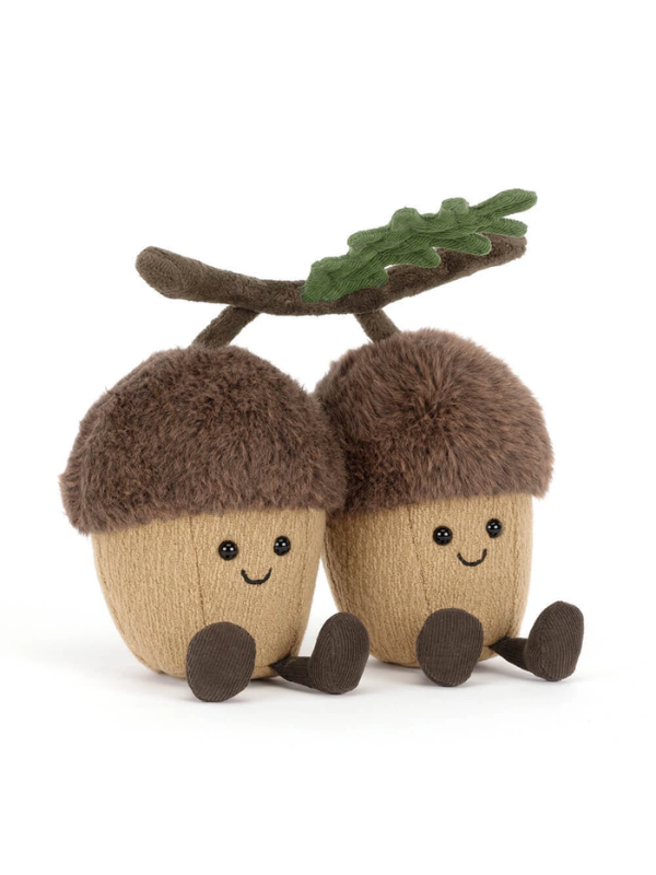Two plush acorn toys sitting side by side on a branch with a green leaf, photographed on a clean white background.