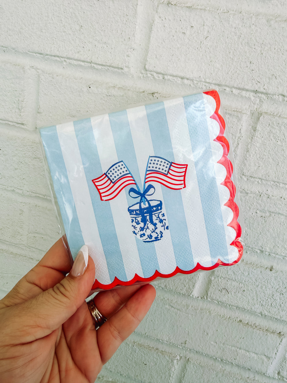 Hand holding a small striped pouch with decorative elements on a light gray tiled background