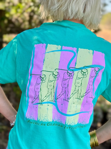 Person wearing a teal t-shirt with a colorful golf graphic on the back, standing outdoors.