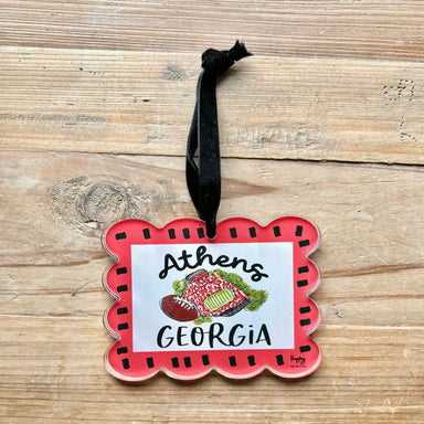 A scalloped acrylic ornament featuring a red border, a white center, and a hand-drawn illustration of a football and Sanford Stadium