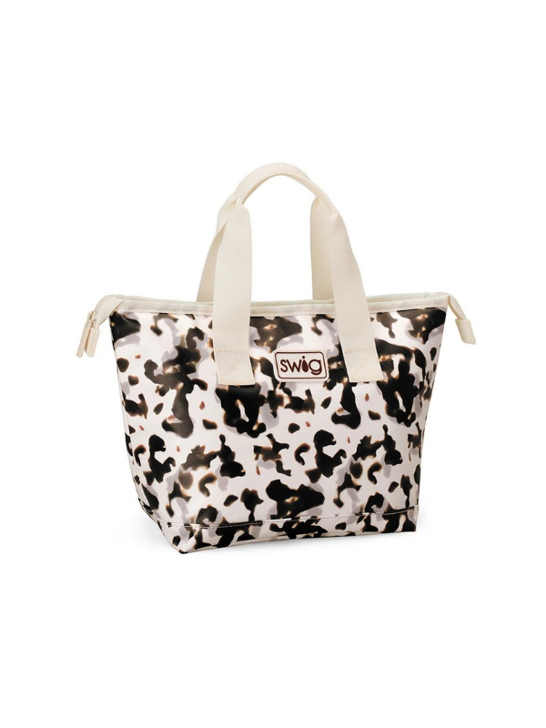 A Swig brand insulated tote bag featuring a black and white cow print pattern with cream-colored handles and zipper trim, shown on a plain white background.