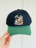 black and green hat with a raccoon in a chair by a bonfire