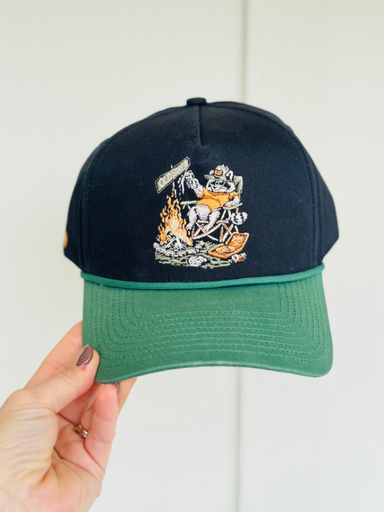 black and green hat with a raccoon in a chair by a bonfire