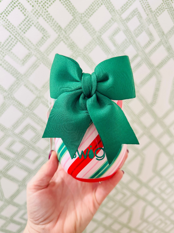 candy-cane-striped gift box topped with a large green satin bow, set against a light green geometric patterned wallpaper background.