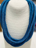 A cobalt blue cotton roping necklace displayed on a white textile stand, featuring a ball-n-eye closure.