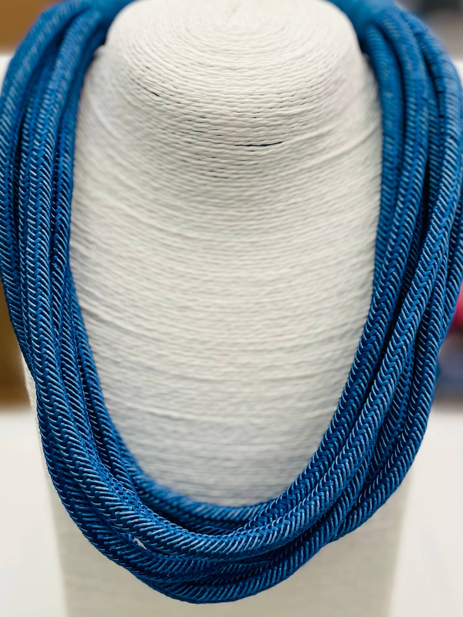 A cobalt blue cotton roping necklace displayed on a white textile stand, featuring a ball-n-eye closure.
