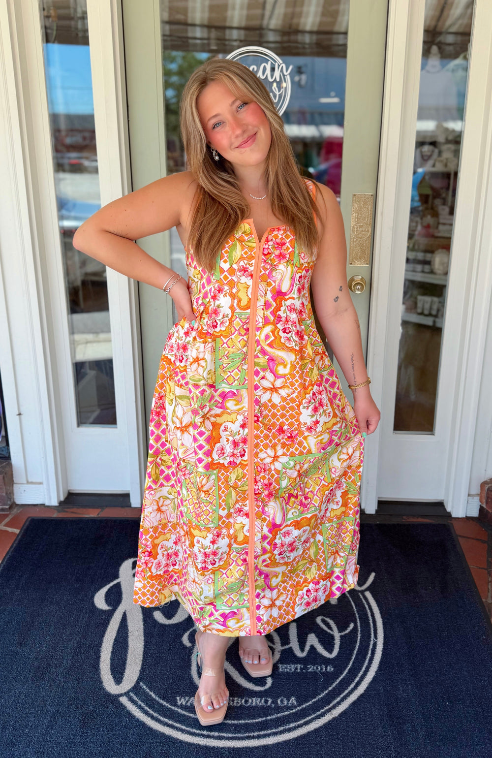 Colorful maxi dress featuring a vibrant patchwork-inspired print in shades of pink, orange, coral, and lime green with floral motifs, wide straps, and a flowing skirt.