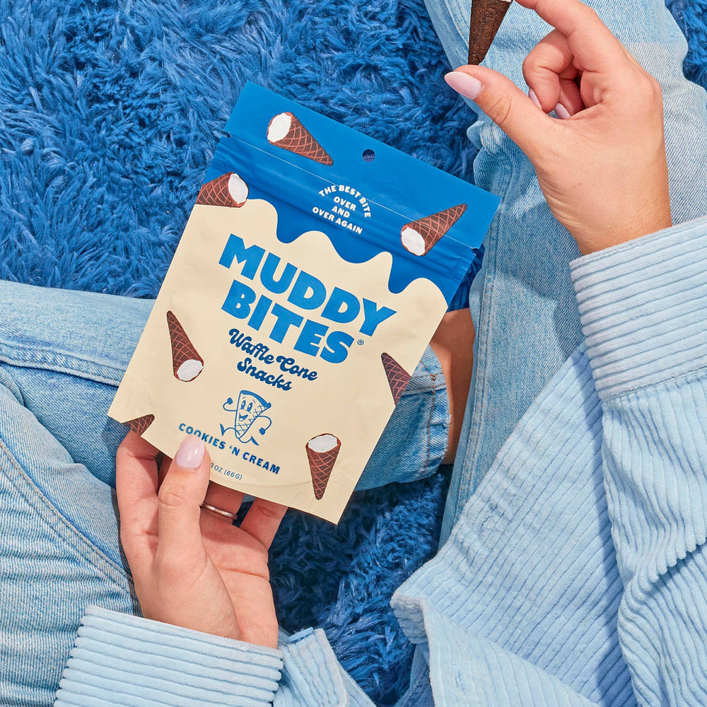 Person holding a package of Muddy Bites Waffle Cone Snacks with a blue textured background