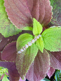 A silver-toned beaded bracelet with clear faceted beads, resting on green and burgundy leaves.