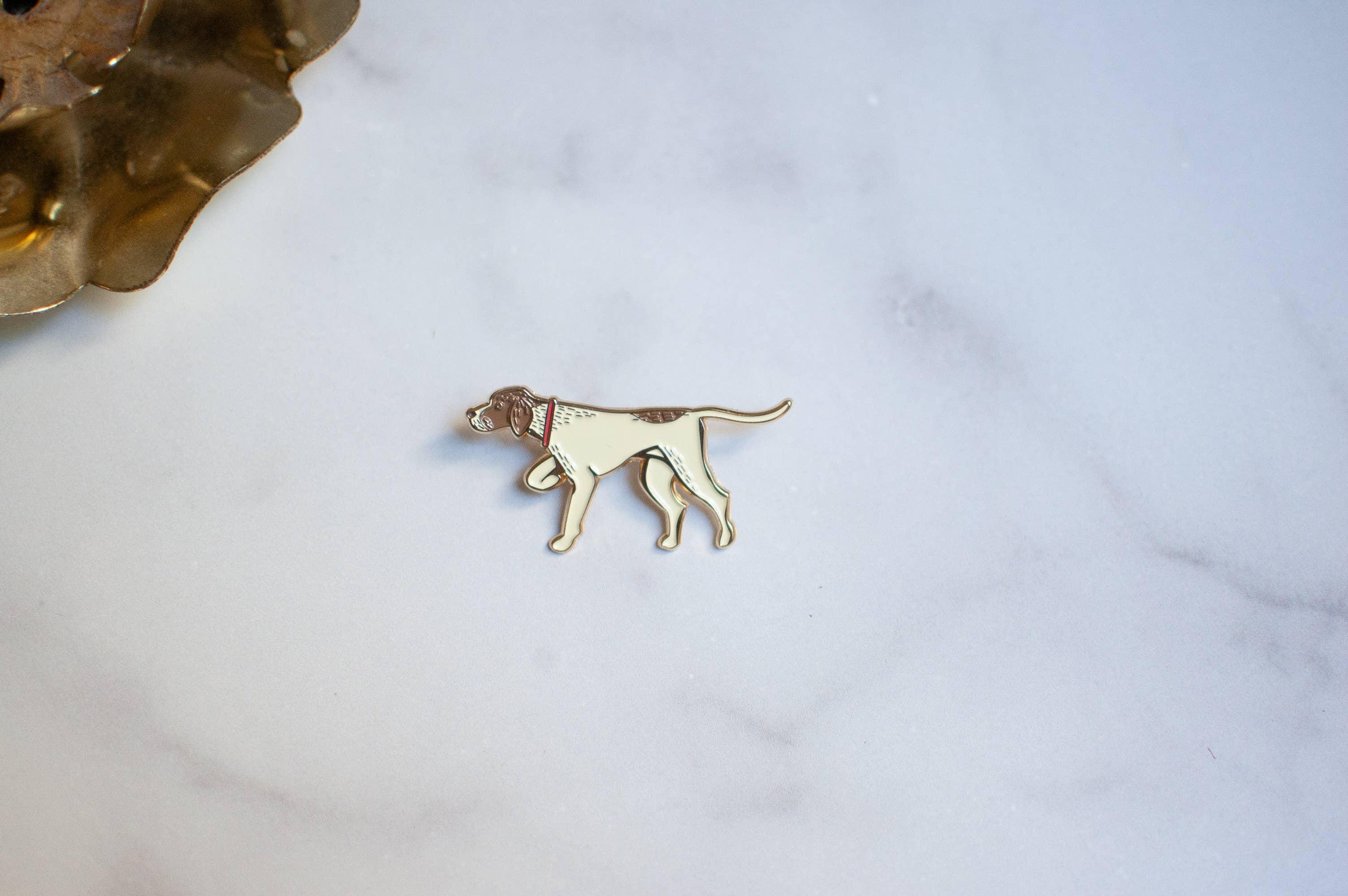 A small dog pin in gold-tone metal with a cream enamel fill