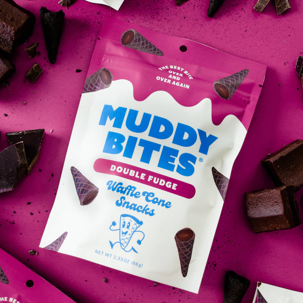 Muddy Bites Double Fudge Waffle Cone Snacks packaging on a pink background with chocolate pieces.