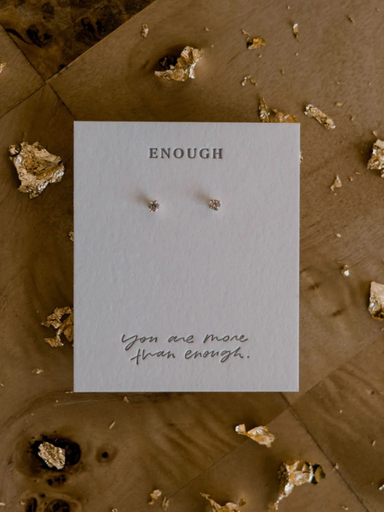 Pair of earrings on a card with 'ENOUGH' and 'You are more than enough' text, surrounded by decorative stones.