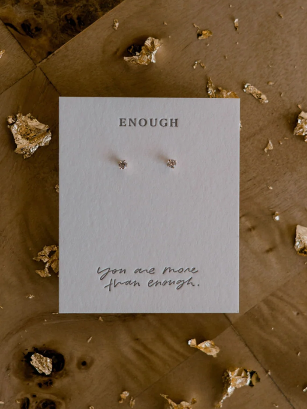 Pair of earrings on a card with 'ENOUGH' and 'You are more than enough' text, surrounded by decorative stones.