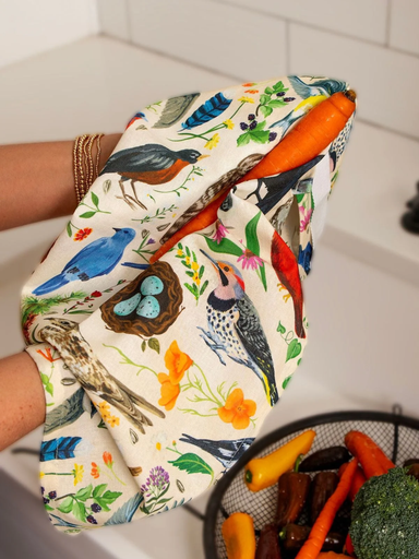 Kitchen tea towel with colorful bird and floral illustrations, featuring various songbirds and botanical details on a neutral background.