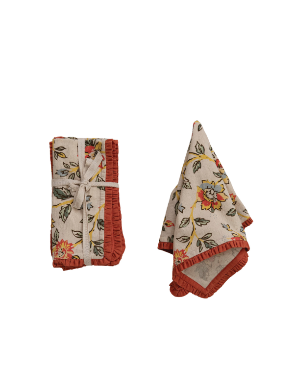 Two folded cotton napkins with a floral vine print on a cream background and rust-colored ruffled trim, shown on a plain white background.