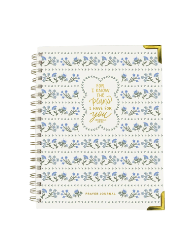 A spiral-bound prayer journal with a white cover decorated with blue flowers, green leaves, and gold foil lettering that reads 'FOR I KNOW THE PLANS I HAVE FOR YOU' and 'PRAYER JOURNAL' at the bottom.