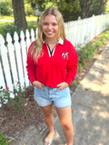 A red long-sleeve polo-style top with a white collar, black trim, and a small sequin embroidered logo on the left chest by Brianna Cannon
