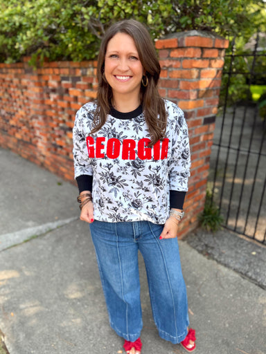 A white long-sleeve top with a black floral toile print and large red 'GEORGIA' lettering across the chest by Brianna Cannon