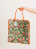 A hand holding a green patterned tote bag with orange handles and trim against a plain white background. The bag features a repeating botanical and bird print in green, pink, and beige.