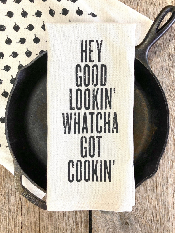 Kitchen towel with text over a cast iron skillet on a wooden surface