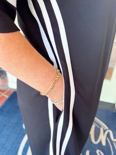 Woman wearing a black midi dress with white striped sleeve and side details paired with a purple beaded necklace and sandals.