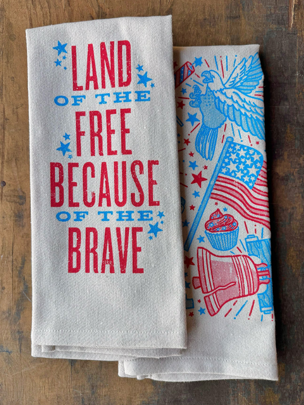 Two towels on a wooden surface, one with patriotic text and the other with an eagle and flag design.