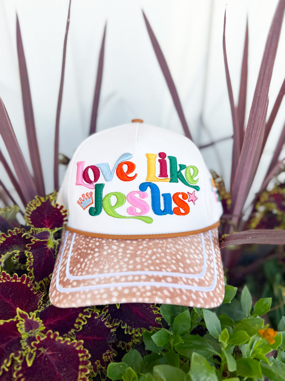 White trucker hat with colorful embroidered “Love Like Jesus” lettering, spotted tan brim, John 13:34 side embroidery, and colorful faith-inspired embroidered icons on the back.
