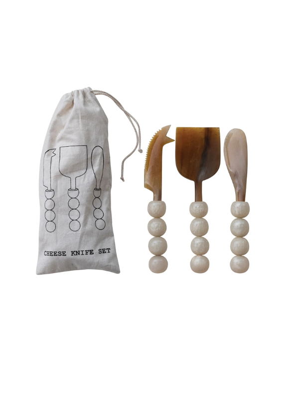 A cheese knife set with three wooden tools featuring white beaded handles, shown next to a beige drawstring pouch printed with 'CHEESE KNIFE SET'.