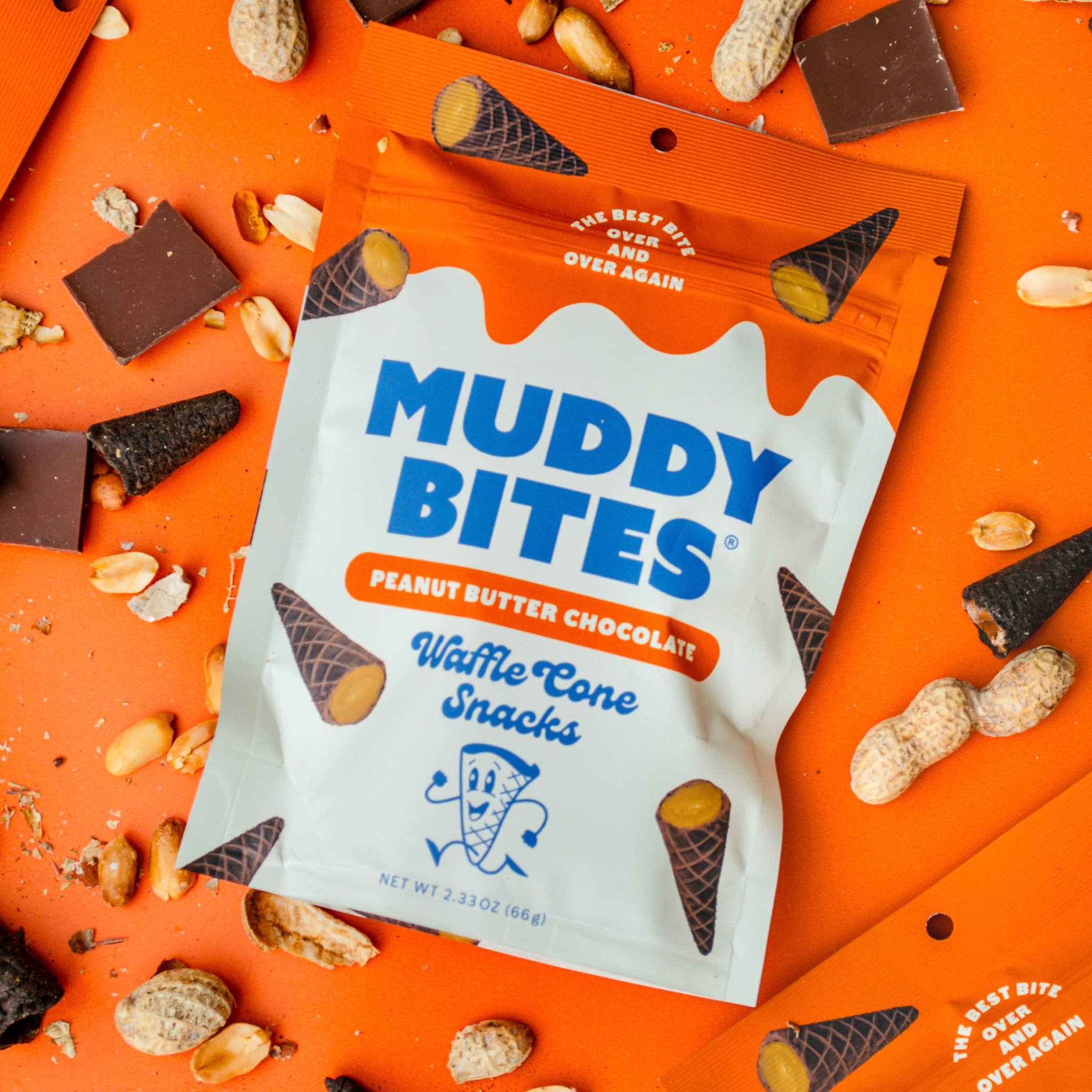 Muddy Bites peanut butter chocolate waffle cone snacks packaging on an orange background with scattered peanuts and chocolate pieces.