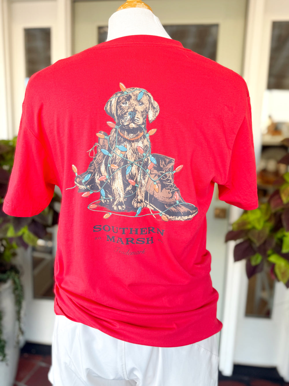  This bright red Southern Marsh tee features a Christmas-ready pup wrapped in colorful string lights and sitting between a pair of boots. 