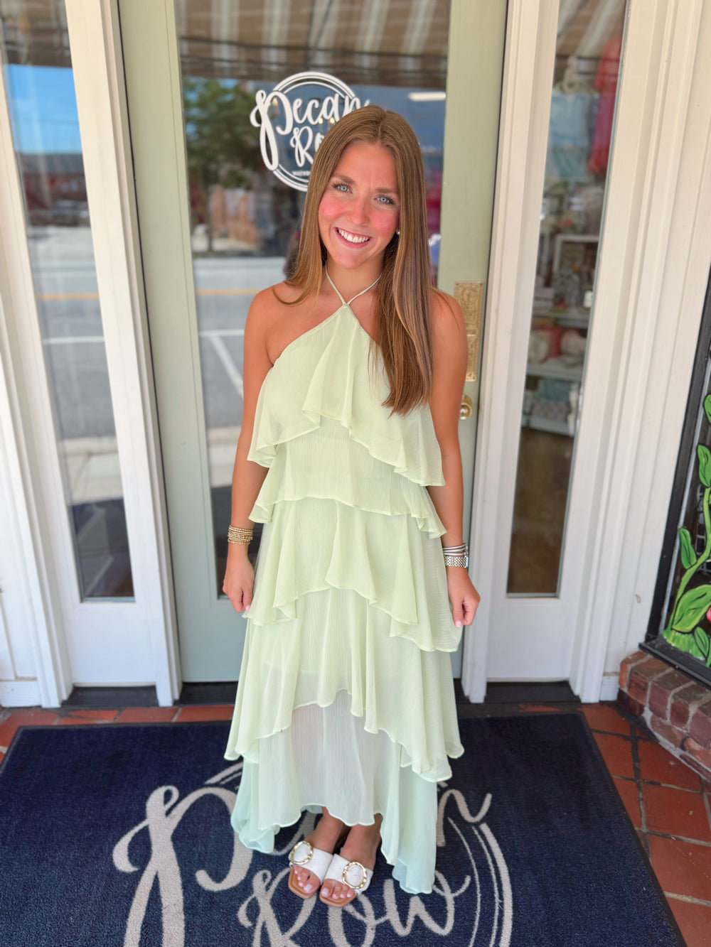 Woman in a light green dress standing in front of a store entrance.