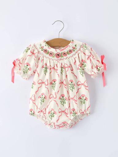 Baby romper with floral and bow pattern on a hanger against a white background