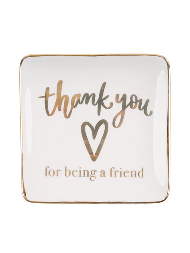 A white ceramic trinket tray with metallic gold lettering that reads 'Thank You For Being A Friend' and a simple heart symbol between the words.