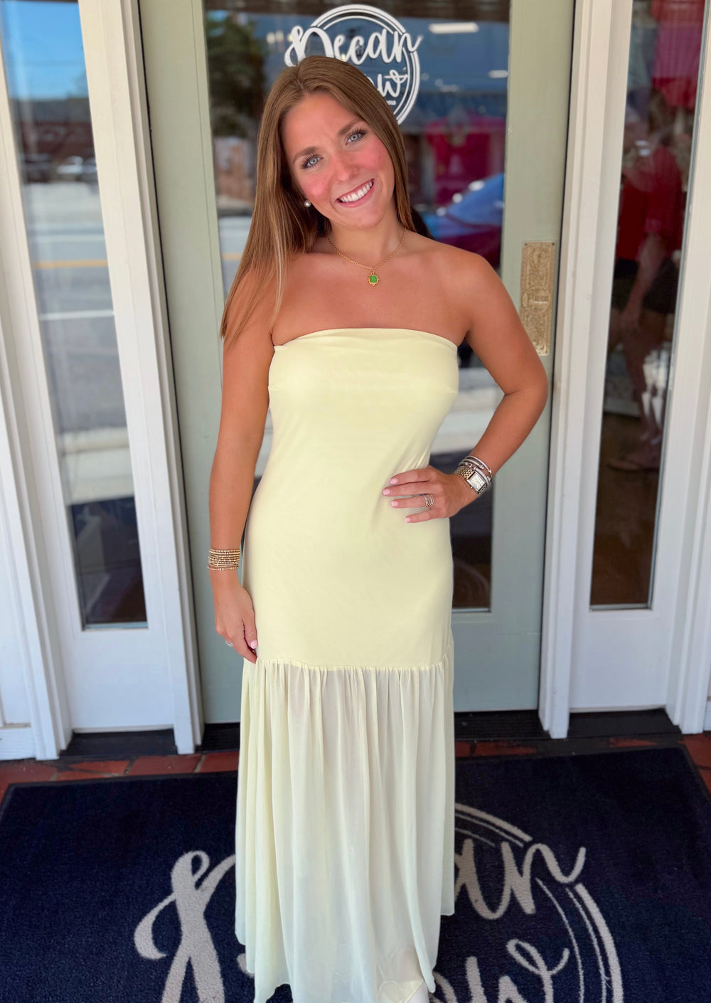 Butter-yellow strapless maxi dress featuring a fitted silhouette with a flowing gauzy hem panel, styled with gold jewelry for an elegant summer occasion look.