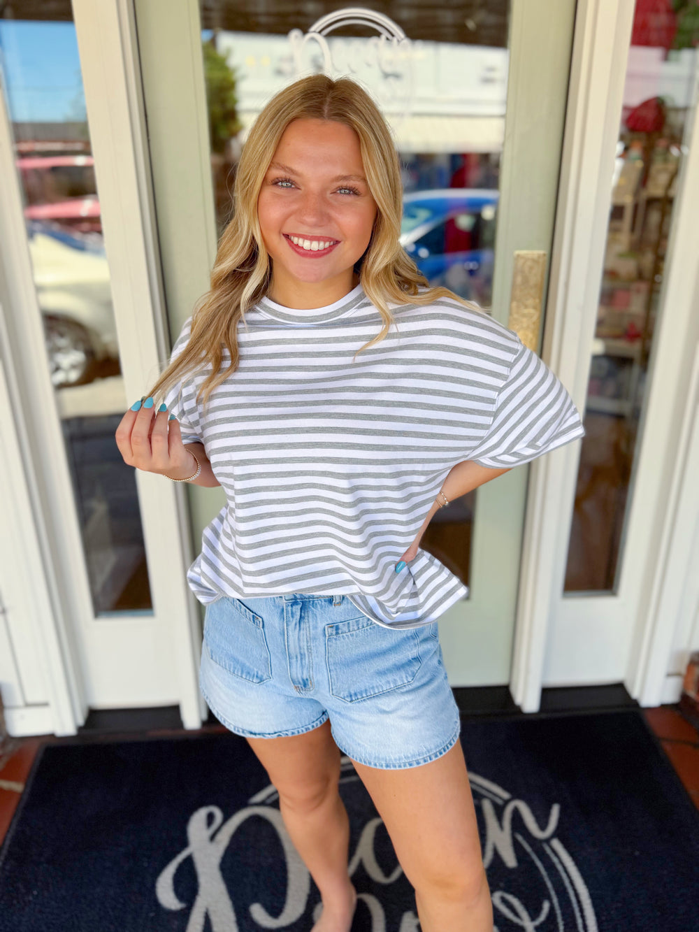 Woman wearing a gray and white striped oversized short sleeve tee paired with light wash denim shorts.
