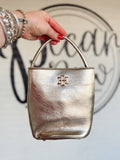  This structured bucket-style handbag features a metallic finish, rounded top handle, and polished gold-tone logo detail. 