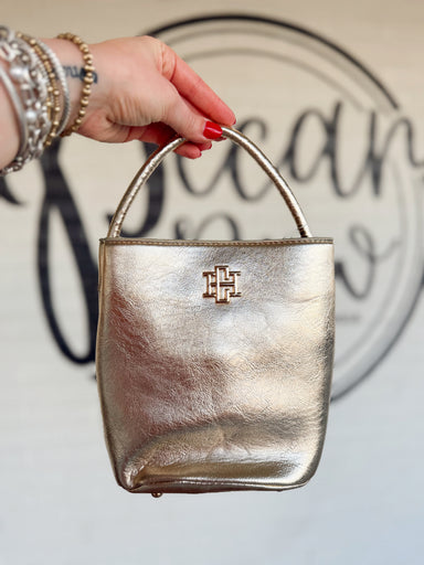  This structured bucket-style handbag features a metallic finish, rounded top handle, and polished gold-tone logo detail. 