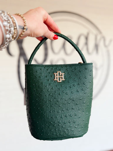 This structured bucket-style handbag features an ostrich-inspired textured finish, rounded top handle, and polished gold-tone logo detail.