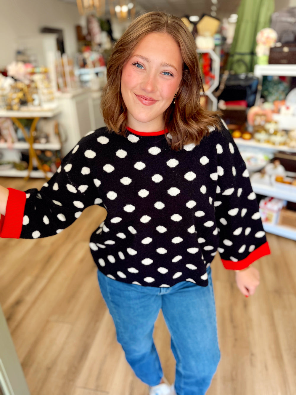  This black knit sweater features an allover cream polka dot pattern with bold red contrast trim at the neckline and cuffs. 