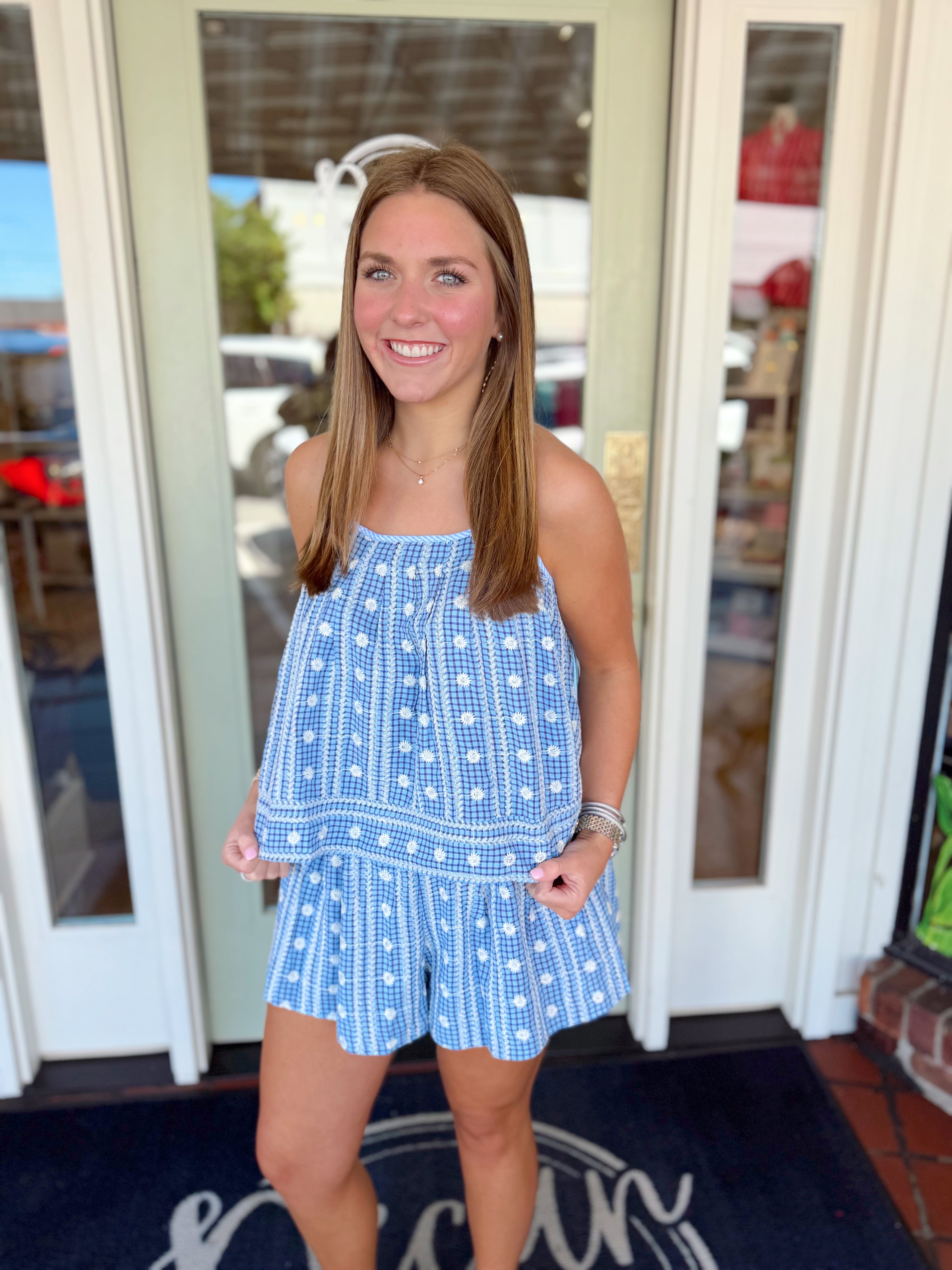 Woman wearing a blue and white floral gingham matching set with a sleeveless flowy top and coordinating shorts.
