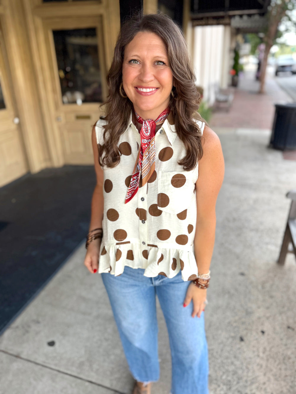 A sleeveless cream button-up blouse with brown polka dots.