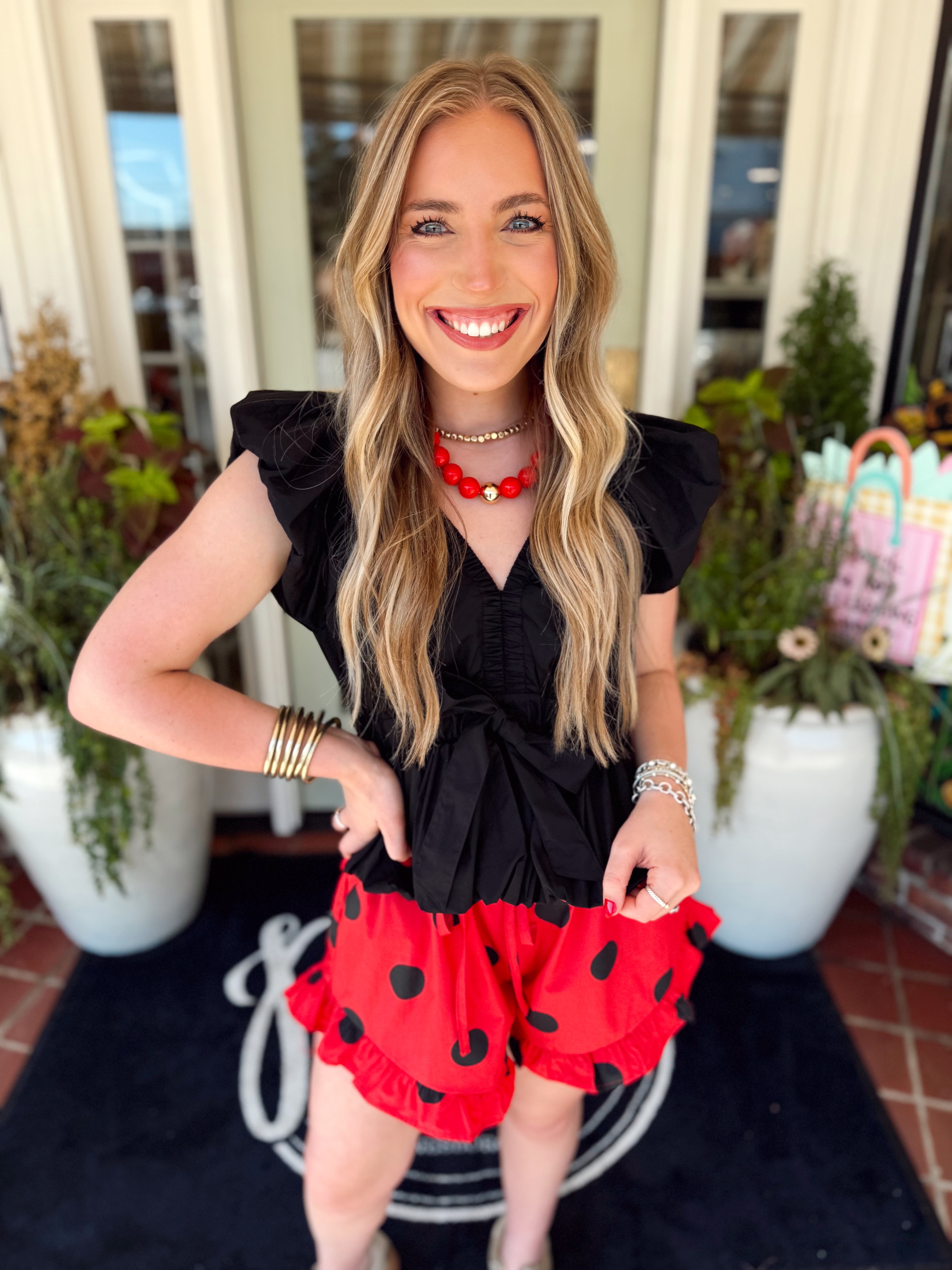 Black sleeveless top with a v-neckline, a cinched waist, and a bow detail on the front of the shirt