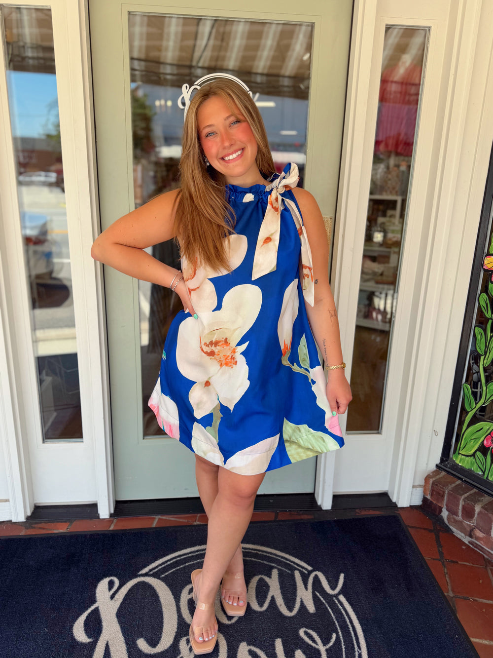 Cobalt blue sleeveless swing dress featuring oversized white magnolia flowers, an adjustable tie-neck detail, and a relaxed, elegant silhouette.