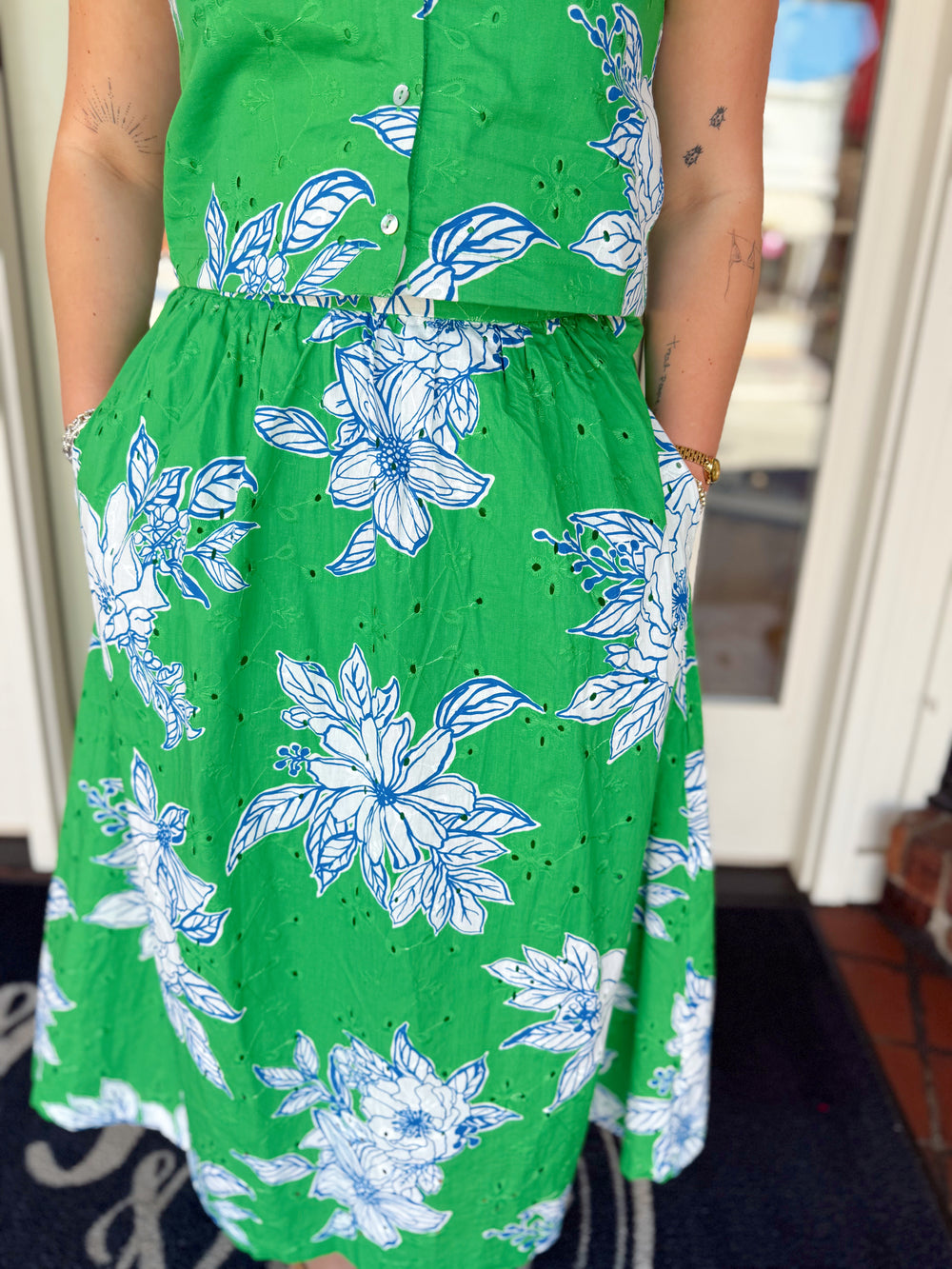 Close-up of a green floral midi dress with blue and white floral print, eyelet embroidery detail, button-front design, and side pockets.