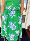 Close-up of a green floral midi dress with blue and white floral print, eyelet embroidery detail, button-front design, and side pockets.