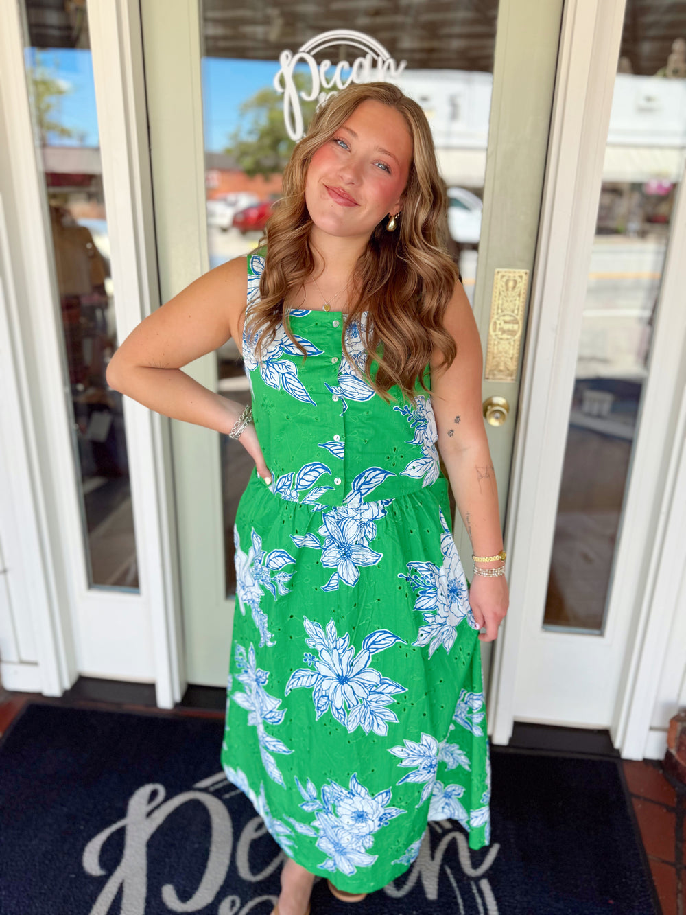 Woman wearing a green floral midi dress with blue and white floral print, sleeveless design, button-front detail, and eyelet embroidered fabric.
