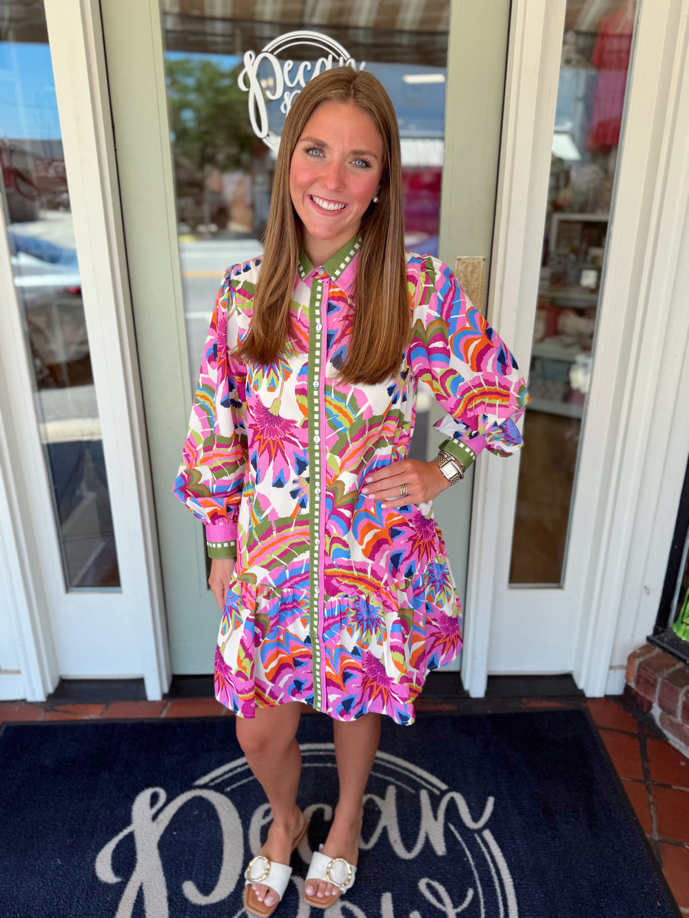 Colorful tropical print shirt dress featuring a button-front design, collared neckline, green contrast trim, long sleeves, and a ruffle hem in vibrant shades of pink, orange, blue, and green.