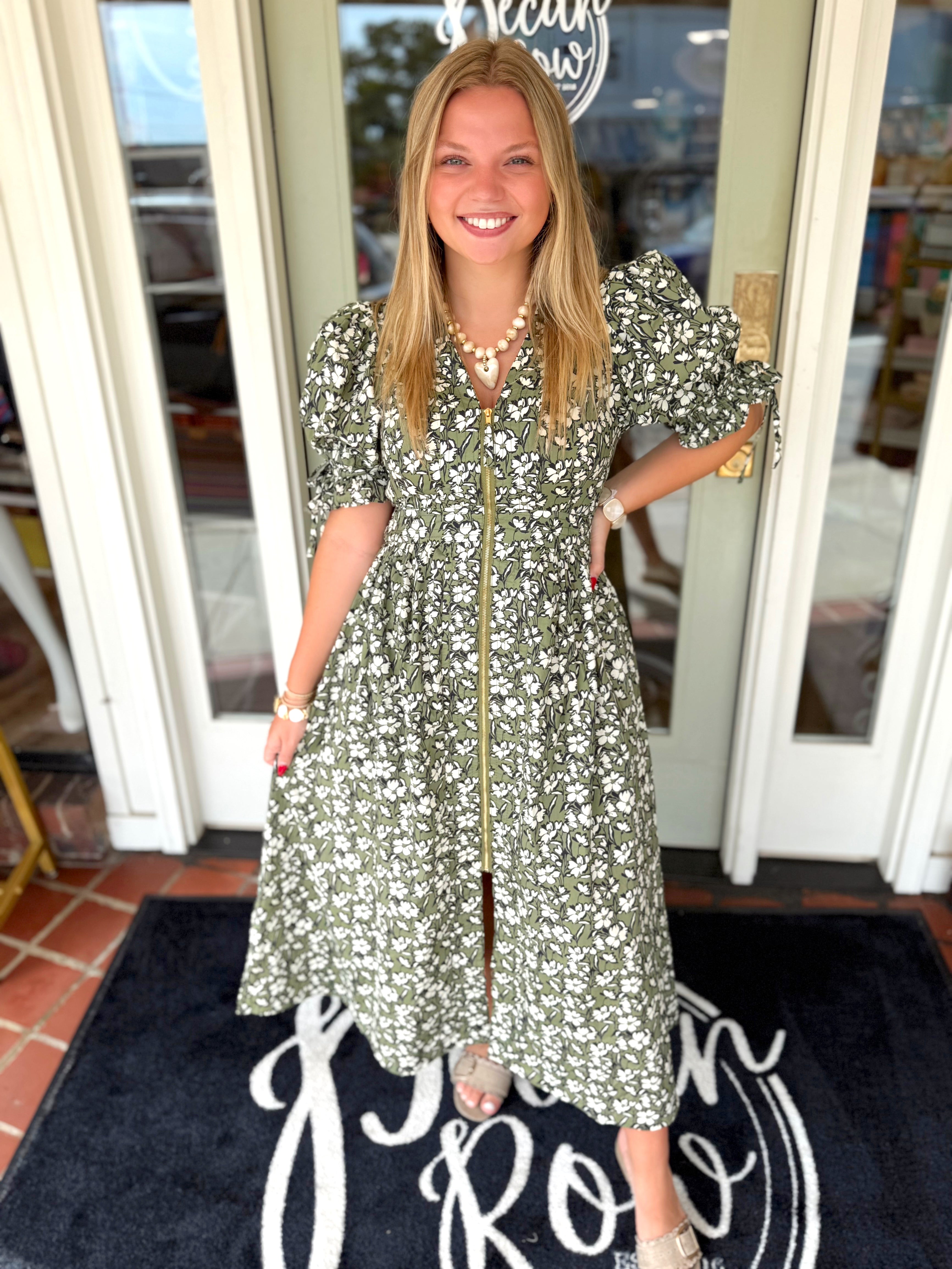 A short-sleeve olive green and white floral print midi dress with a gold front zipper.