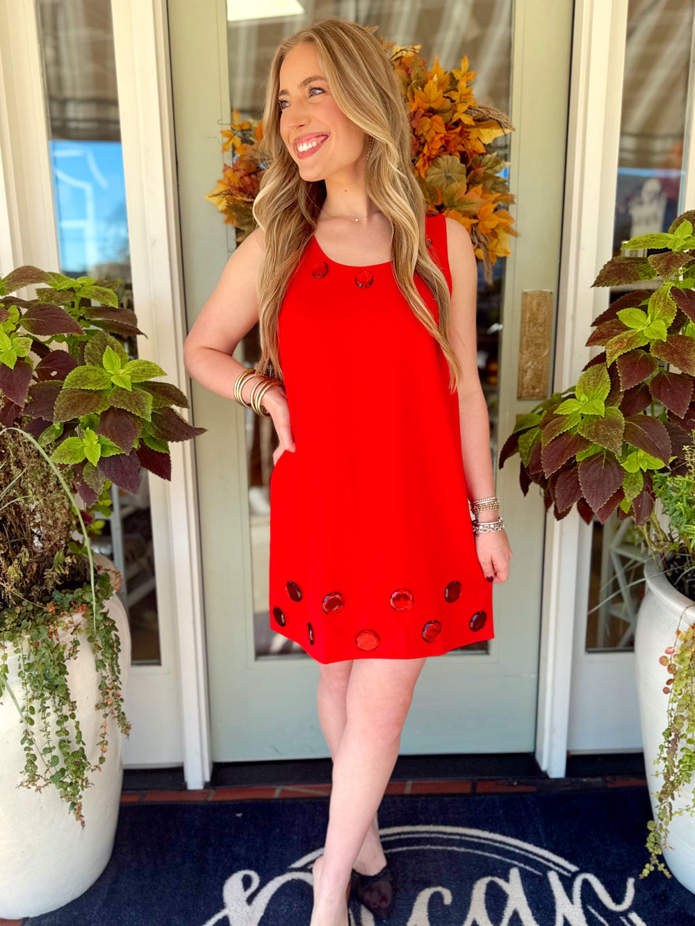  This sleeveless shift dress features a vibrant red color with oversized tonal jewel embellishments around the neckline and hem. 